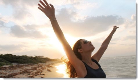 Woman with both hands held high - sunset on a beach